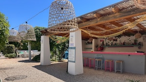 Un espace extérieur abrité, aménagé avec des sièges, un bar, des cages à oiseaux en osier et un sol en gravier.