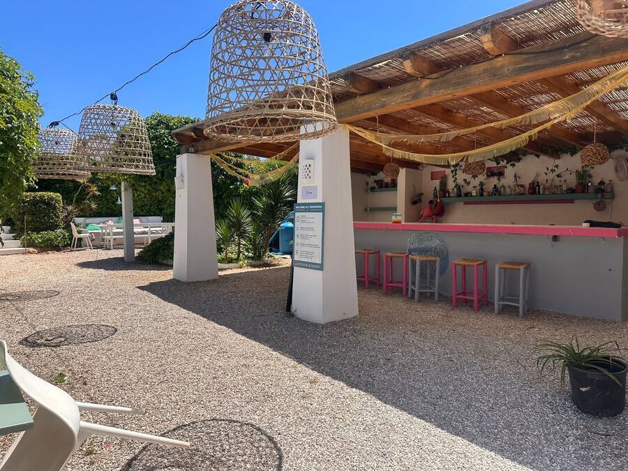 A covered outdoor seating area with a bar, wicker birdcages, and a gravel ground.