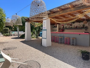 A covered outdoor seating area with a bar, wicker birdcages, and a gravel ground.
