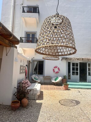 A balcony with a wicker hanging light fixture, a white wall, and a window with a white curtain. - Flamingo by Nest (Santa Eulalia del Rio)