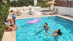 Une piscine avec des personnes dans l’eau, des chaises longues et un ciel dégagé.