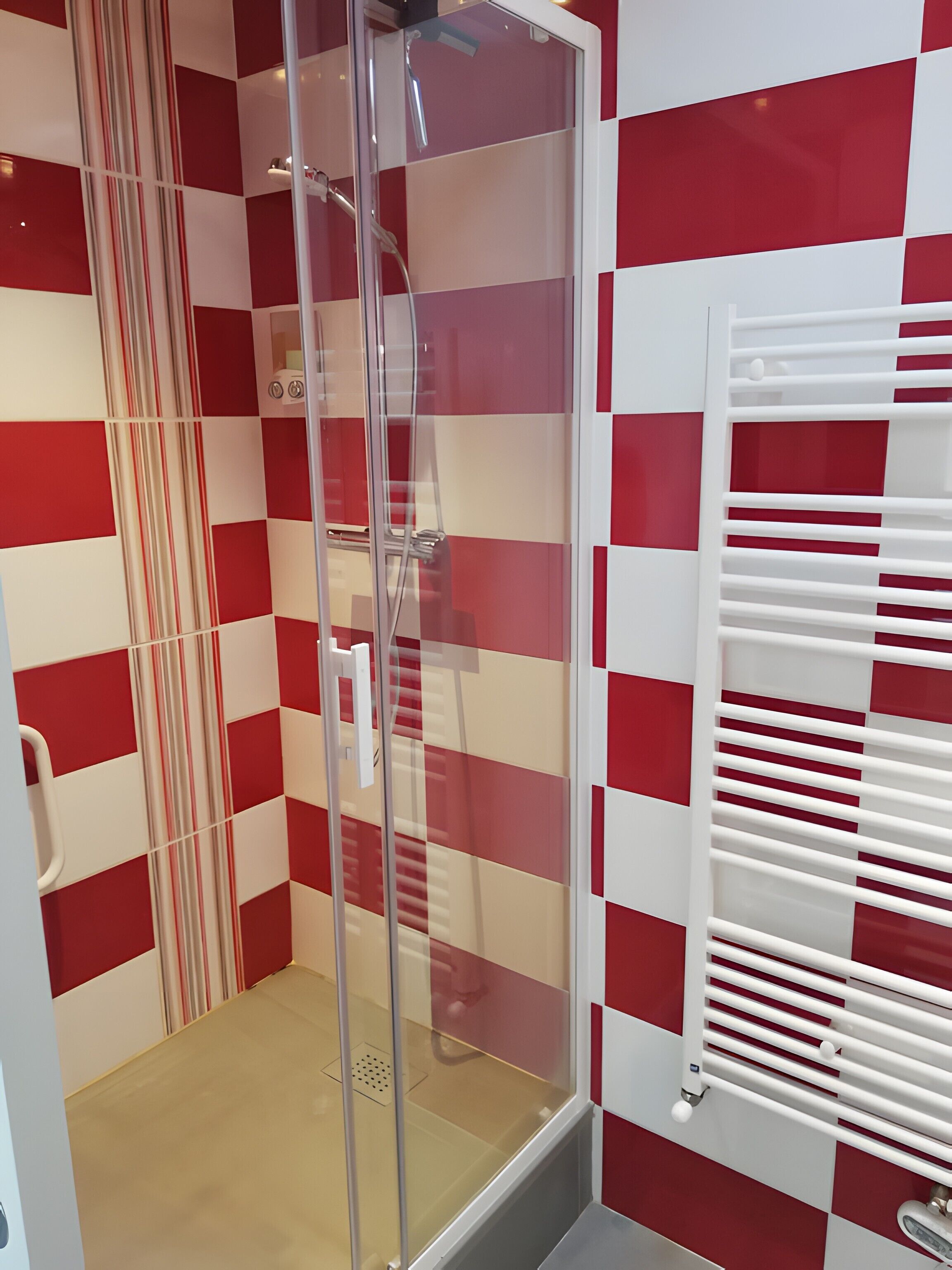 Een badkamer met een douchecabine van glas, een witte handdoekhouder en een rode en witte geruit muurpatroon.