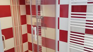 Een badkamer met een douchecabine van glas, een witte handdoekhouder en een rode en witte geruit muurpatroon.