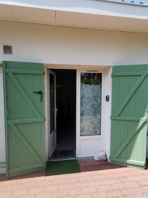 Entrada d'un edifici amb una porta verda i una porta de vidre, un felpudet i un petit escaló que condueix a l'entrada.