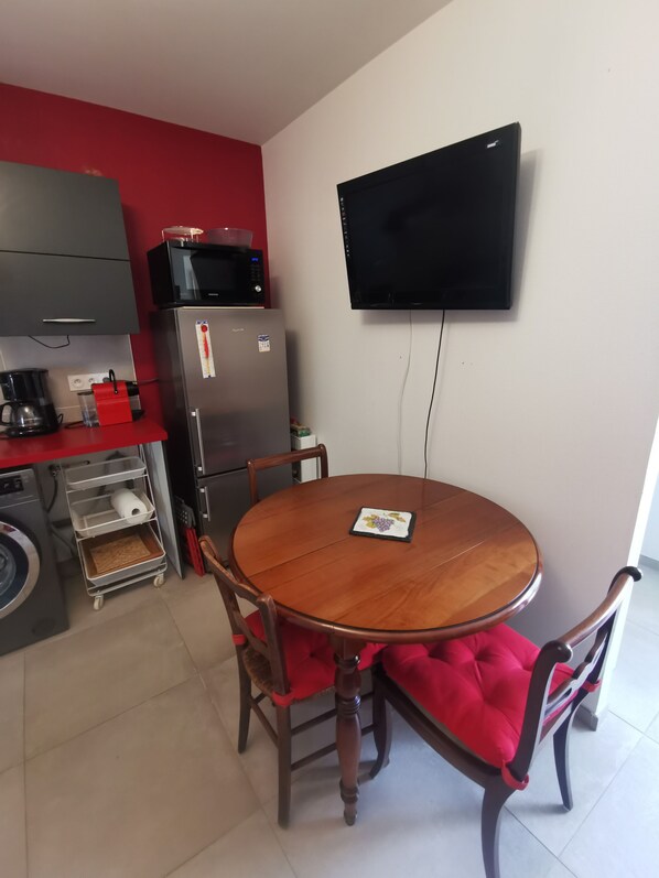 A compact kitchen with a microwave, refrigerator, and a flat-screen TV mounted on the wall.