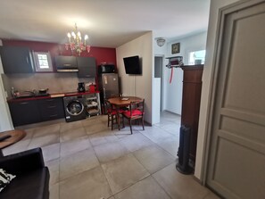 A compact kitchen with a dining area, a washing machine, and a TV mounted on the wall. - 37 m² Apartment with Private Garden and Wi-Fi (Yerres)