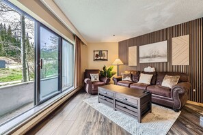 A modern living room with a large sliding glass door, a brown leather sofa set, a wooden coffee table, and a patterned rug. - 2 Studios Steps to Lift, Pool, Hot Tubs & Slopes (Breckenridge)