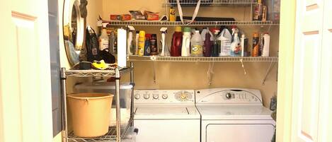 A laundry room with a washing machine, dryer, shelves with cleaning supplies, and a sink with a red mop.