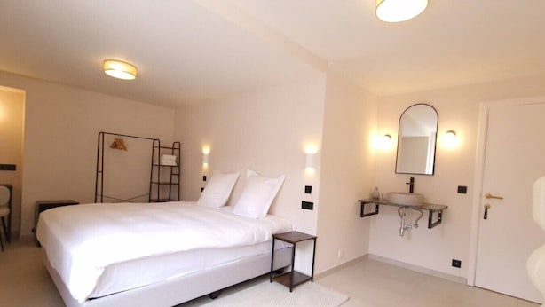 A hotel room with a bed, bedside table, a small desk, a chair, a bathroom with a sink and mirror, and a door. - ROOM N°6 / Deluxe Room in Historic City Centre • Private External Bathroom (Bruges)