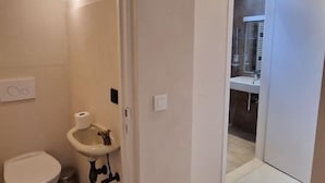 A bathroom with a toilet, sink, and shower. There is a door leading to another room. - ROOM N°6 / Deluxe Room in Historic City Centre • Private External Bathroom (Bruges)