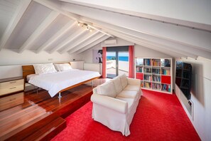 Un dormitorio con cama, sofá, estantería y vista al mar.
