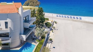 Ein modernes Hotel mit Pool, Blick auf den Strand und einer Reihe blauer Sonnenschirme.