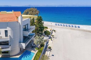 Ein modernes Hotel mit Pool, Blick auf den Strand und einer Reihe blauer Sonnenschirme.