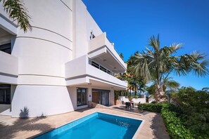 Ein modernes Gebäude mit Swimmingpool, Sitzgelegenheiten im Freien und Palmen.
