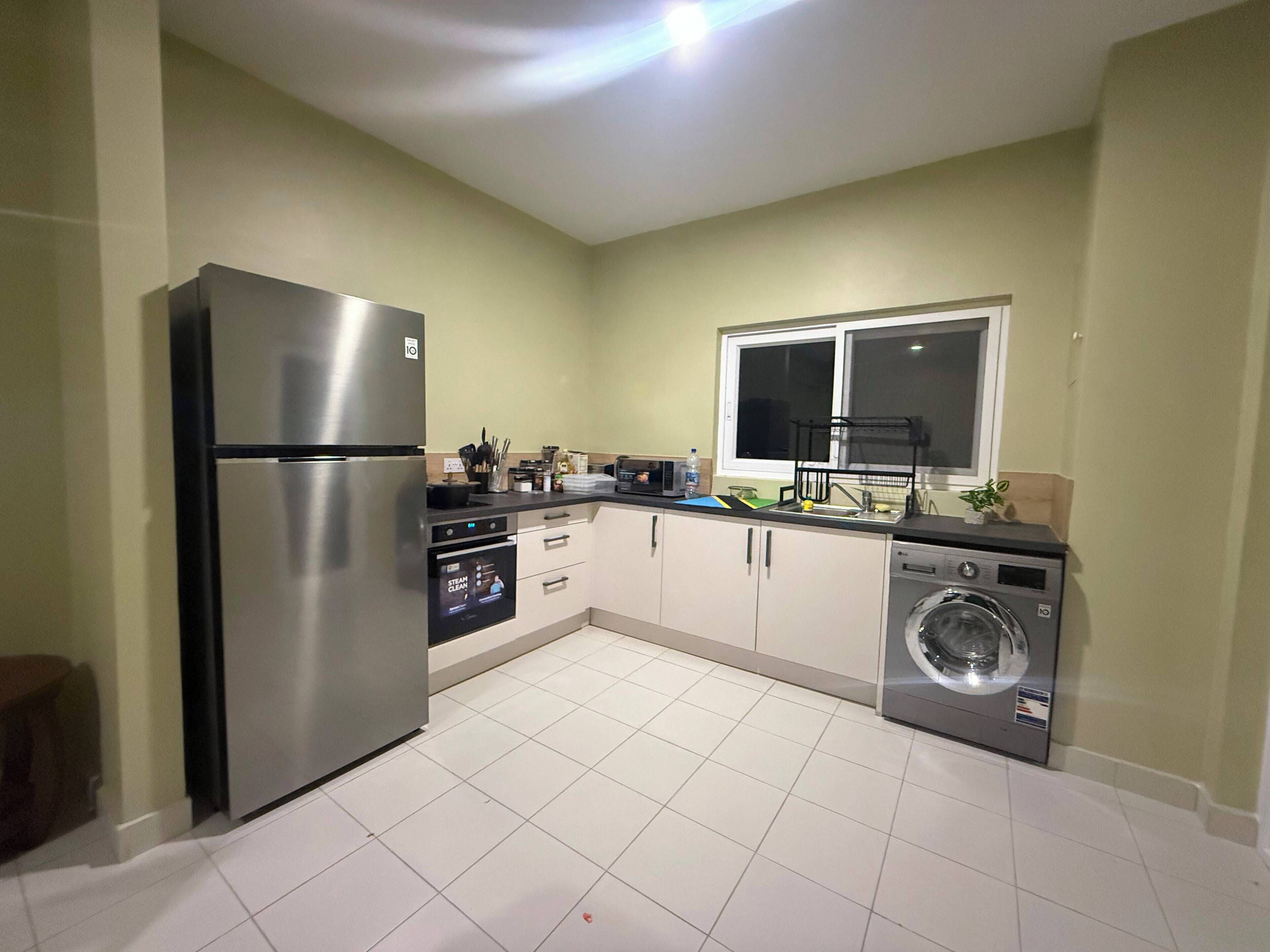 A compact kitchen with a stainless steel refrigerator, a dishwasher, and a washing machine.