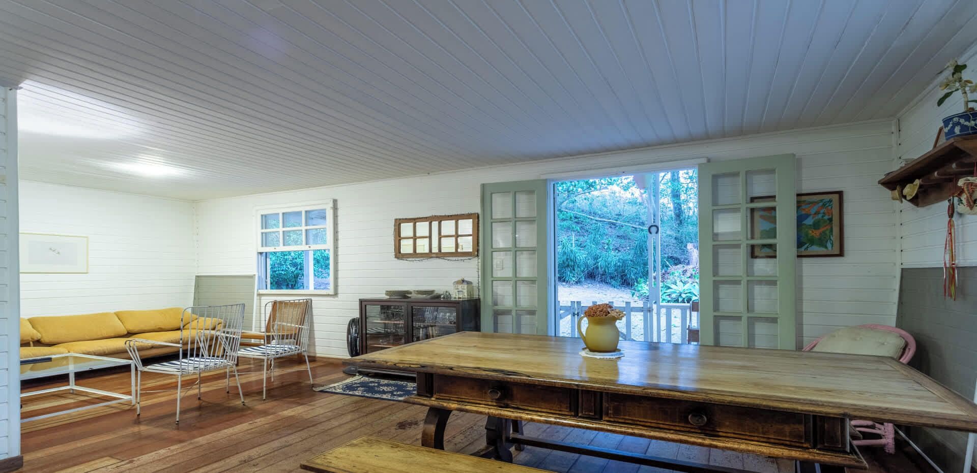 A spacious room with a wooden dining table, a sofa, and a window overlooking a garden.