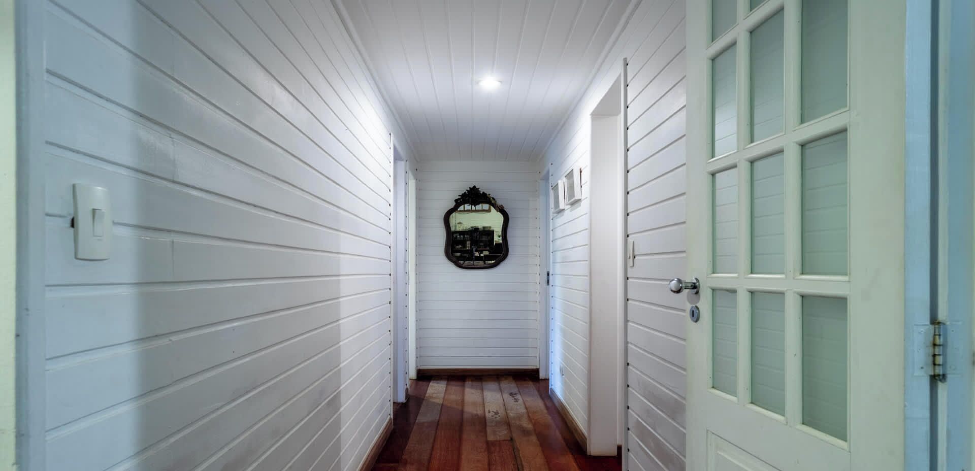 A narrow hallway with white paneling, a wooden floor, and a door with glass panels.