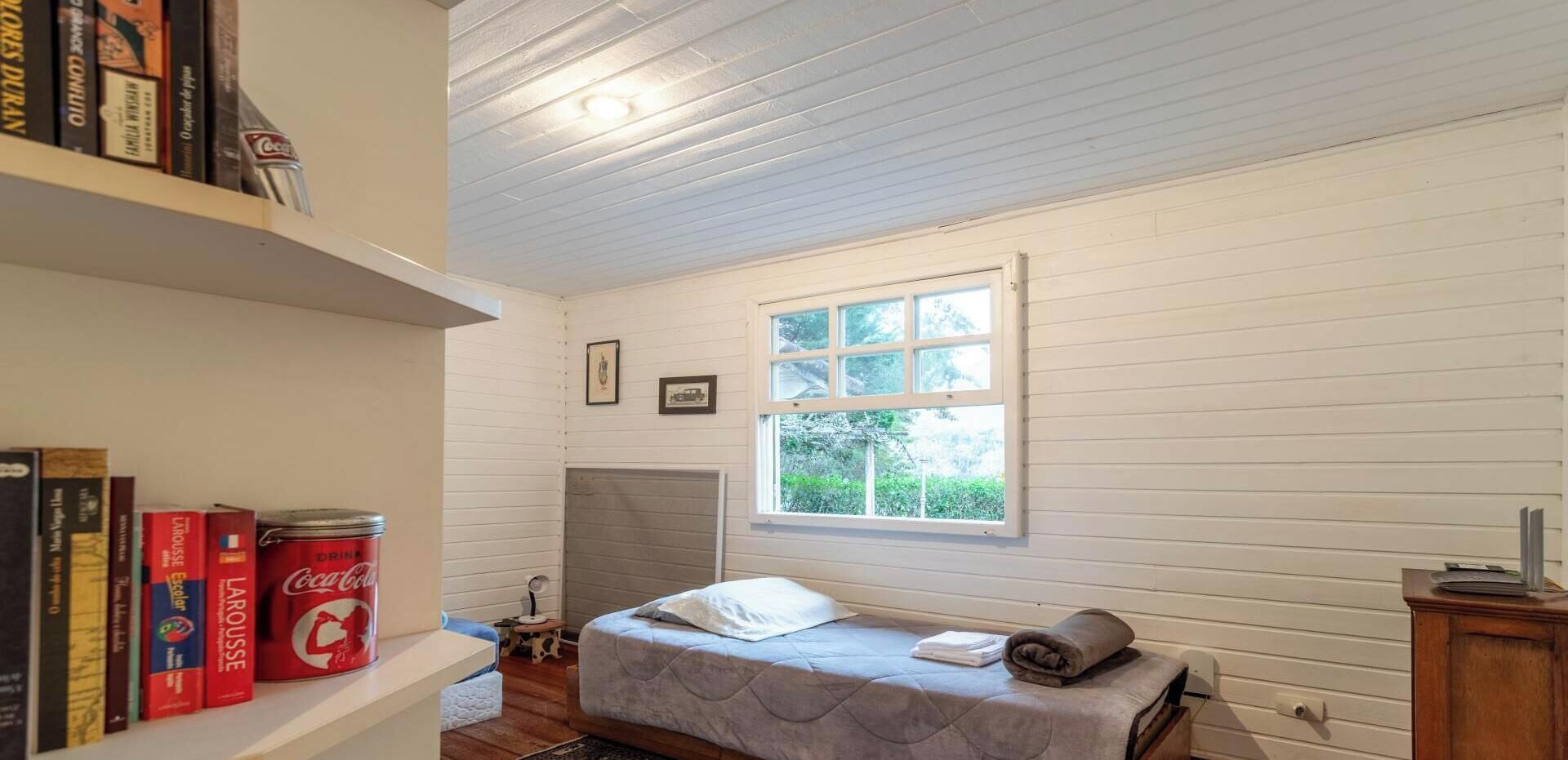 Een slaapkamer met een enkel bed, een raam, een boekenkast en een radiator.