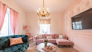 Ein Wohnzimmer mit einem grünen Sofa, einem rosa Sofa, einem Holztisch und einer Chandelieber.