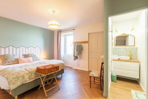 A bedroom with a bed, bedside table, suitcase, and a chair. - Vrbo Property (Montaigu-Vendée)