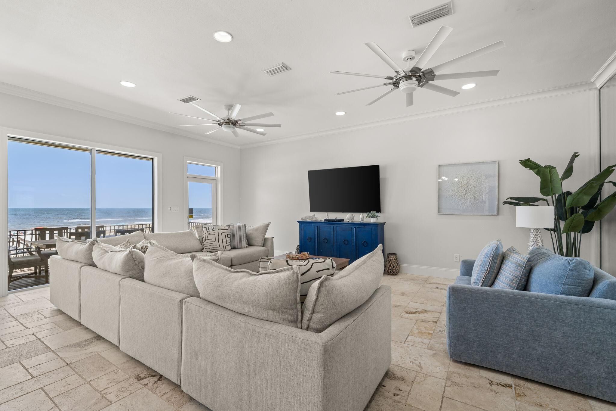 A spacious living room with a large gray sofa, a blue armchair, and a flat-screen TV mounted on the wall.