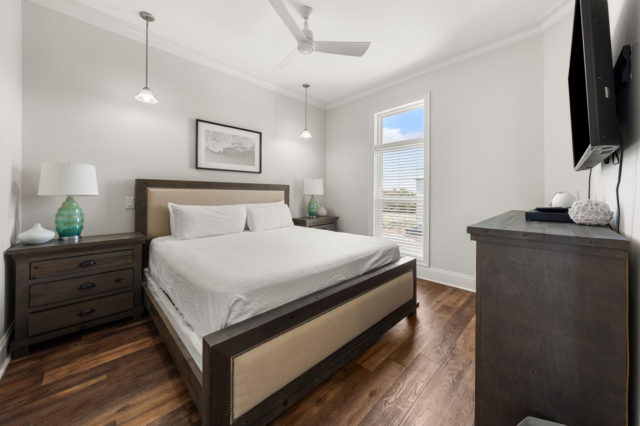 A bedroom with a bed, nightstands, a dresser, a ceiling fan, and a window with blinds.