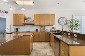 A modern kitchen with wooden cabinets, a large island, and a clock on the wall. - Hammock Dunes East (Orange Beach)