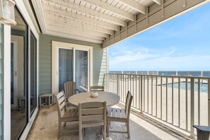 A covered outdoor area with a table and chairs, a sliding glass door, and a view of the beach. - Hammock Dunes East (Orange Beach)