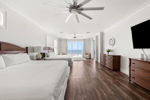 A hotel room with a large bed, a smaller bed, a dresser, a television, and a view of the beach. - Hammock Dunes East (Orange Beach)