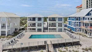 Ein Strandhotel mit Swimmingpool, mehreren Balkonen und einer Holzterrasse mit Liegestühlen.