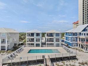 A beachfront hotel with a swimming pool, multiple balconies, and a wooden deck with sun loungers. - Hammock Dunes East (Orange Beach)