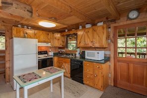 Une cuisine rustique en bois, équipée d’un réfrigérateur, d’une cuisinière, d’un four à micro-ondes et de meubles de rangement en bois.