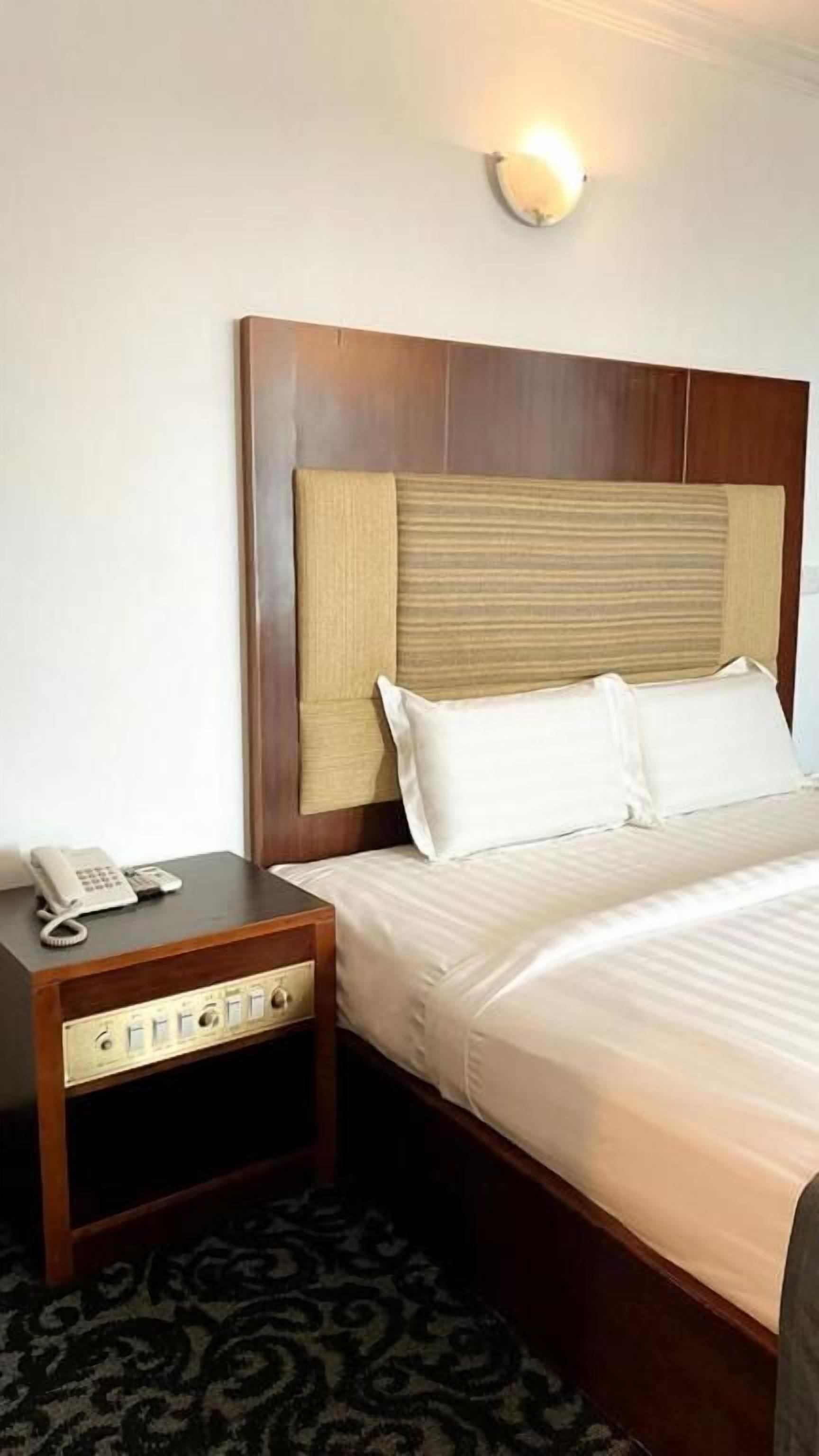 Une chambre d’hôtel avec une tête de lit en bois, un téléphone sur la table de chevet et un tapis à motifs.