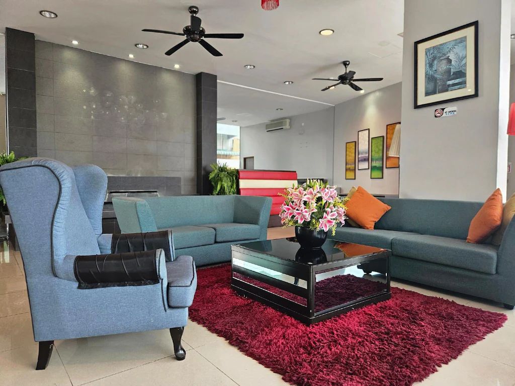 A modern living room with a blue sofa, a glass coffee table, and a red rug. There are ceiling fans and a fireplace in the background.