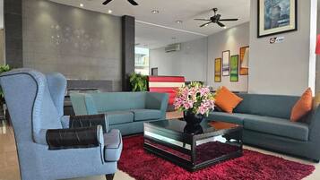 A modern living room with a blue sofa, a glass coffee table, and a red rug. There are ceiling fans and a fireplace in the background.