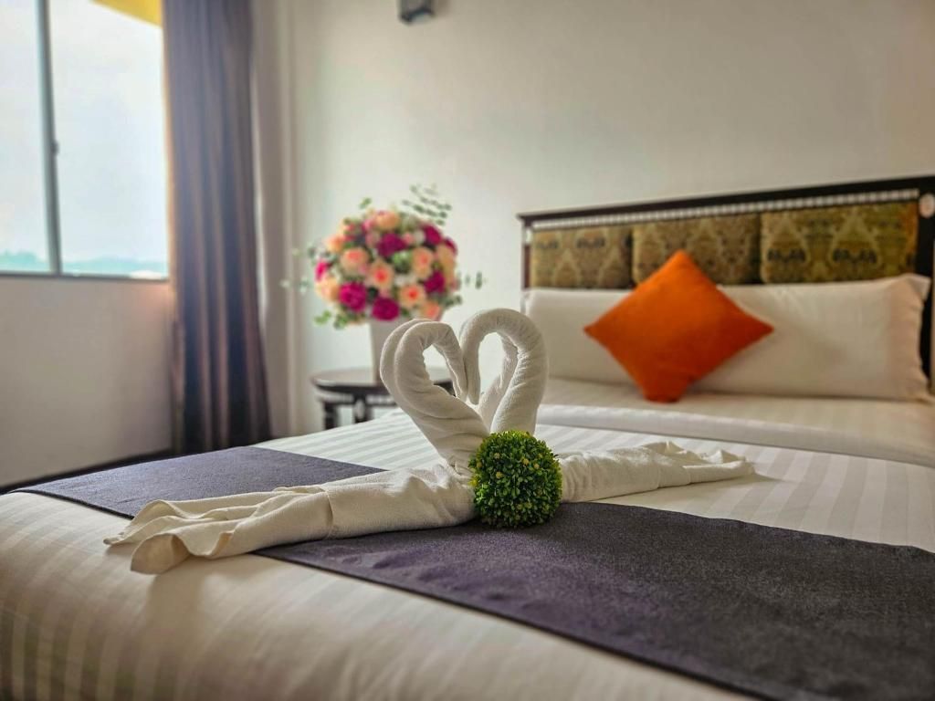 Een netjes opgemaakt bed met een decoratieve handdoeksculptuur en een bloemstuk.