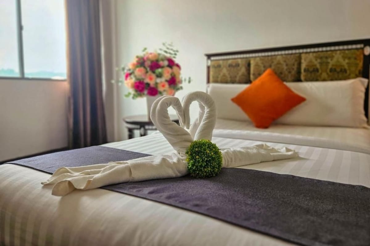 Una cama bien hecha con una escultura de toallas y un arreglo floral.