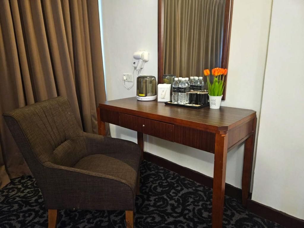 A hotel room with a wooden desk, a chair, a hairdryer, a kettle, bottled water, and a vase with flowers.