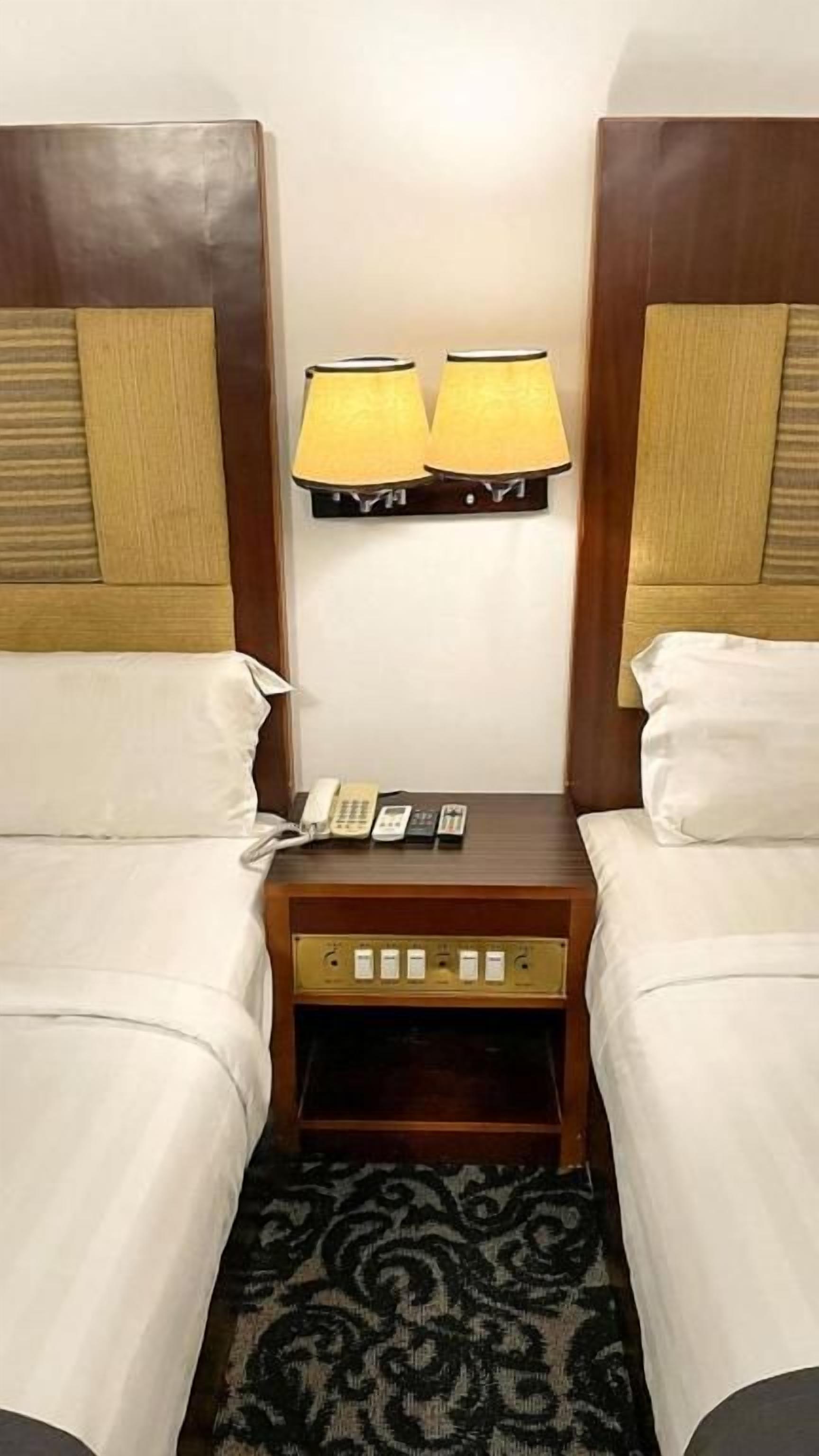 A hotel room with two beds, a nightstand with a lamp, and a telephone.