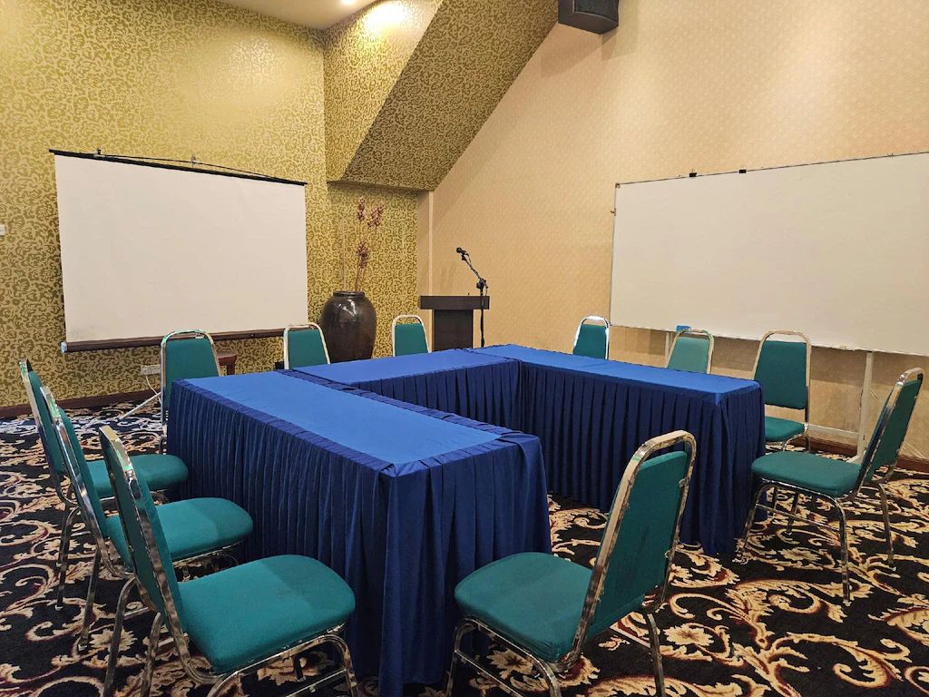 A conference room with a long table, chairs, a podium, and two projection screens.