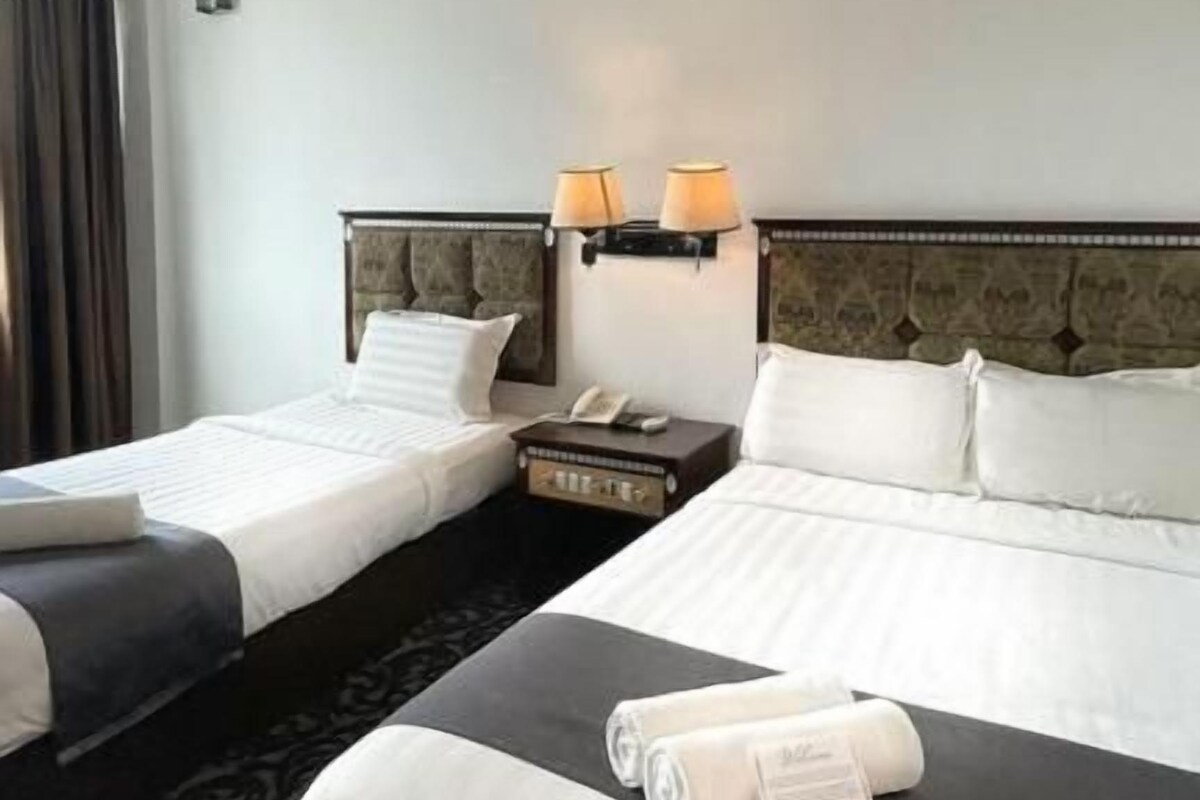 A hotel room with two beds, a bedside table with a lamp, and a telephone.