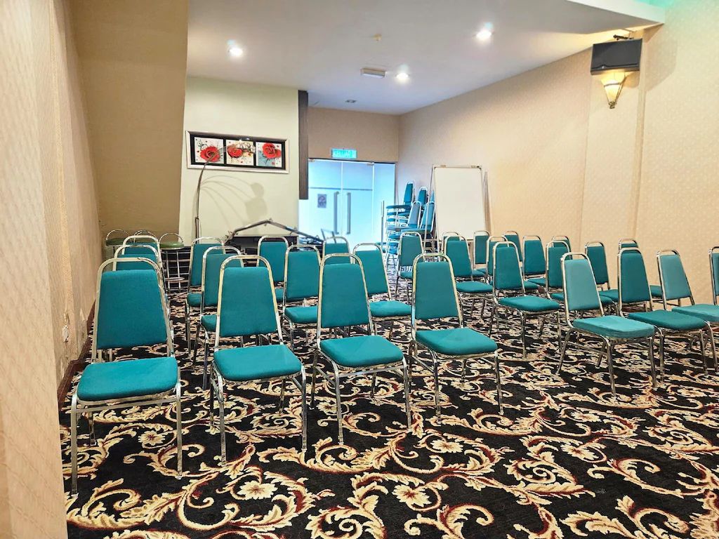 A conference room with rows of teal chairs, a patterned carpet, and a whiteboard.