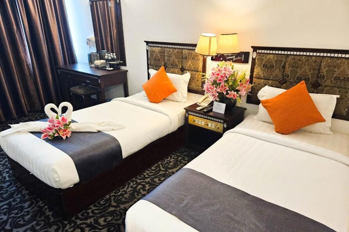 A hotel room with two beds, a nightstand with a lamp, and a desk with a chair.