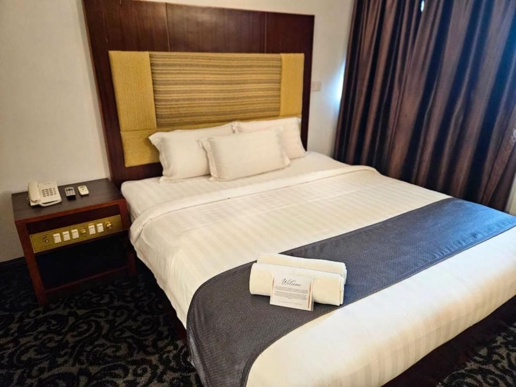 A hotel room with a bed, a nightstand with a phone, and a welcome mat.