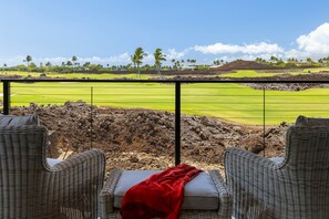 Udsigt over en golfbane fra en balkon med fletstole og et rødt tæppe.