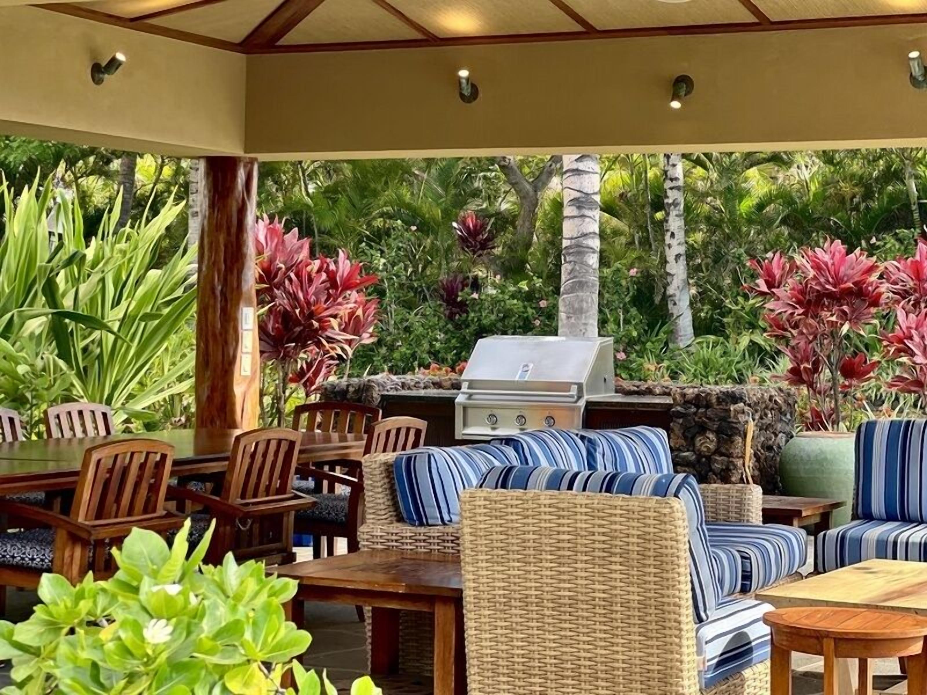 An outdoor patio area with a grill, wicker furniture, and tropical plants.