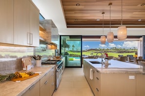 A modern kitchen with a central island, stainless steel appliances, and a view of a golf course. - Exquisite 6BR One Ocean Estate (GE5) at Mauna Lani – Ocean Views & Infinity Pool (Kamuela)