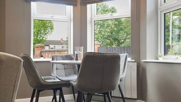 A corner room with two grey chairs, a small table, and a view of a brick building through large windows.
