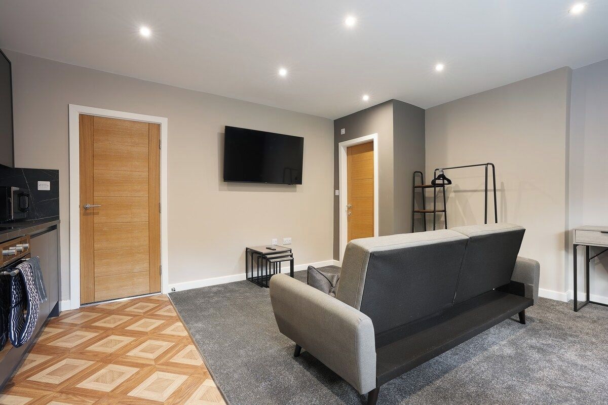 A modern living room with a sofa, a flat-screen TV mounted on the wall, and a wooden door.