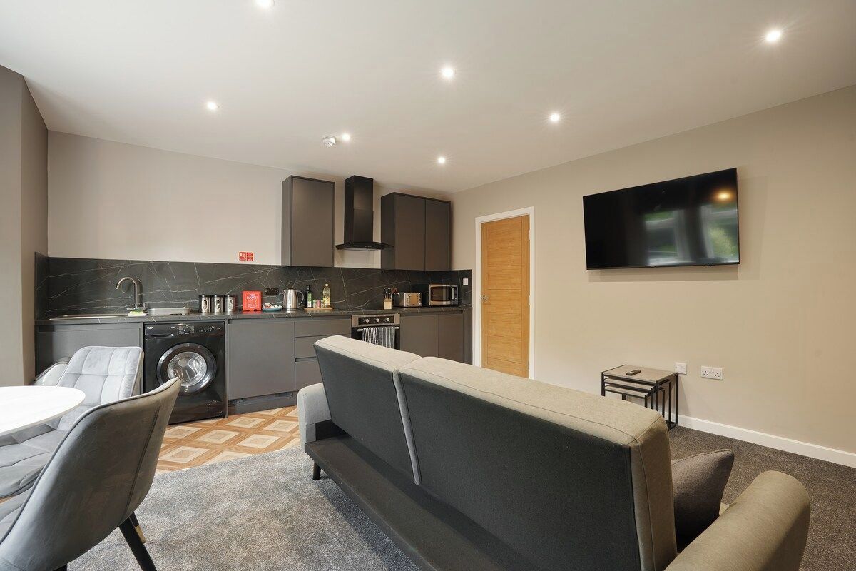 A compact living space with a kitchenette, a sofa, a dining area, and a flat-screen TV mounted on the wall.